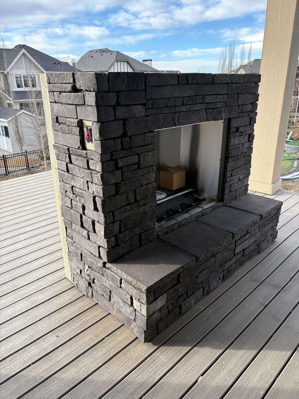 Outdoor stone fireplace and hearth bench on a backyard deck