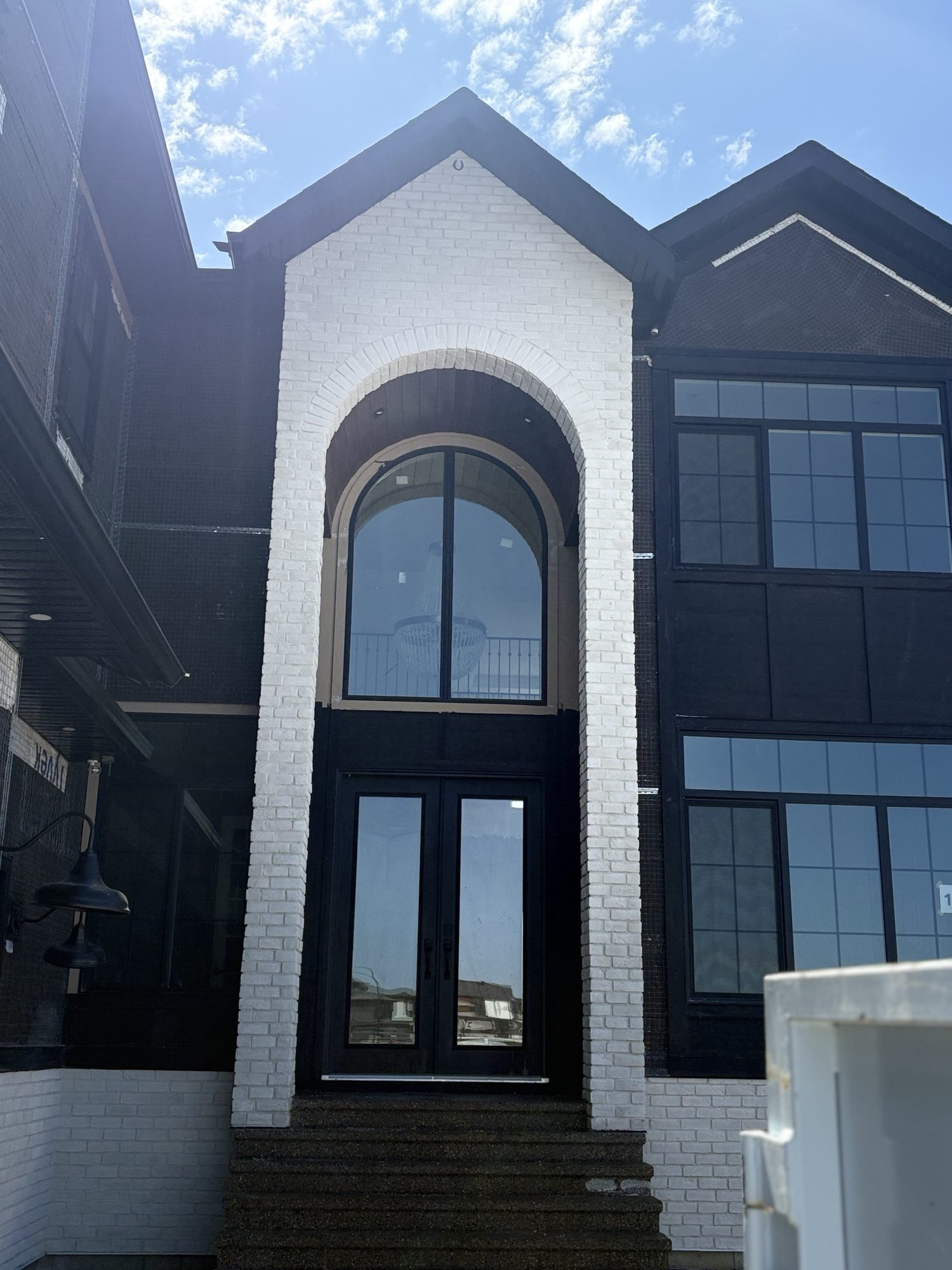 Custom home with tall arched white brick entry framing dark double doors